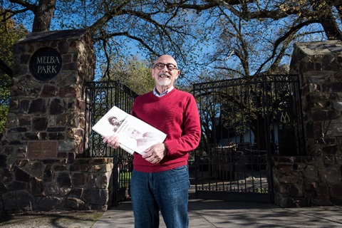 Phil Burton from Lilydale and District Historial Society, in front of the Melba Gates, holding historical books.