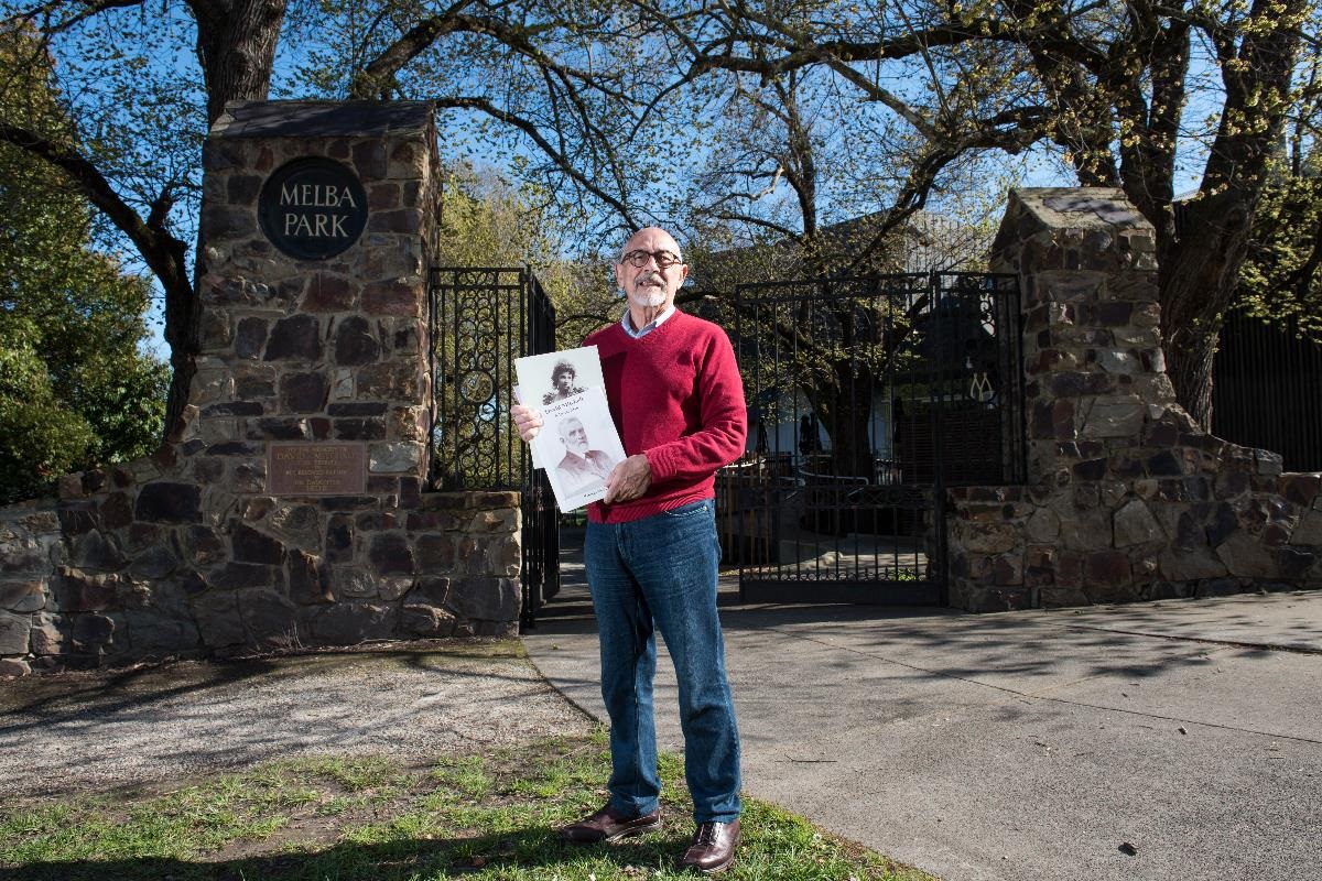 Phil Burton from the Lilydale and District Historical Society in front of the Melba Gates, holding historical books.