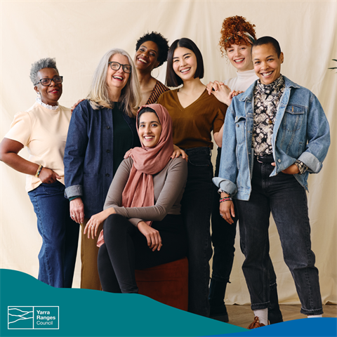 A group of women of different ethnicities and backgrounds stand together, smiling at the camera.