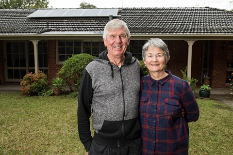 Two people stand outside of a house with a solar panel on top.