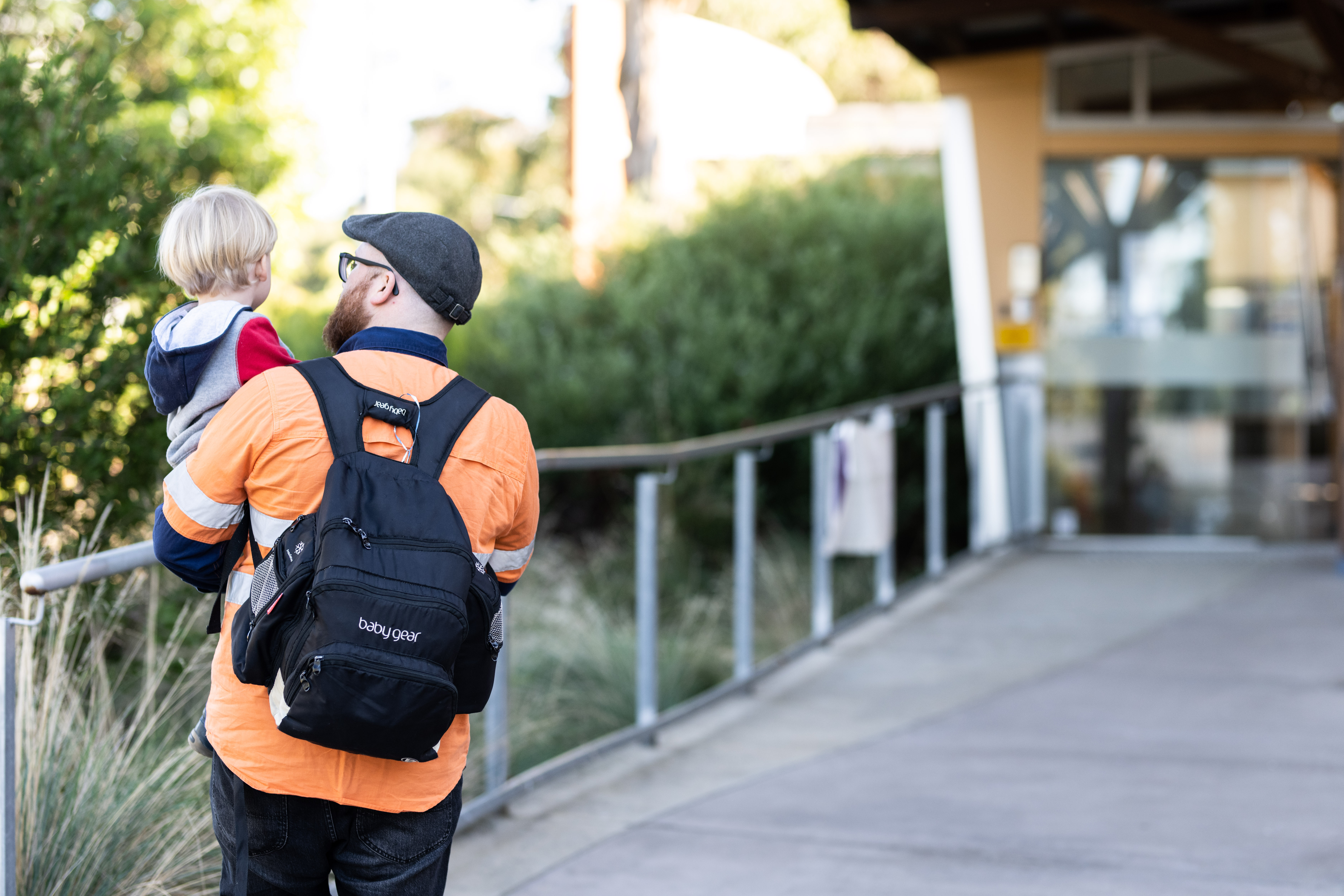A man carrying a child towards a daycare or preschool.
