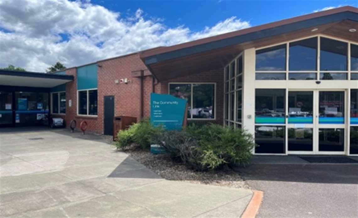 Entrance to a red brick, single storey building with aqua sign reading The Community Link