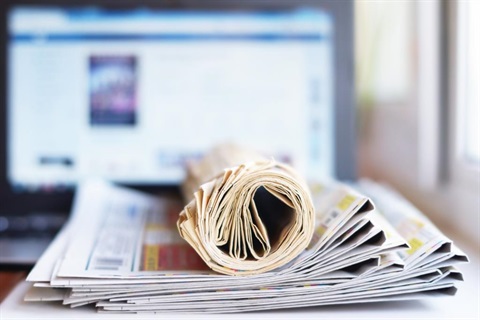 stack of newspapers with computer behind